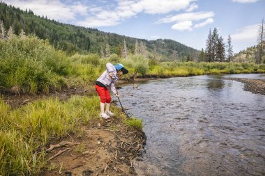 Güneşli bir günde nehir kıyısını gezen bir çocuk.