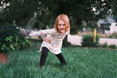 Dışarıda çimenli bir bahçede oynayan neşeli genç kız.