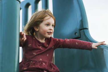 Küçük kız neşeyle oyun parkında kaydırak oynuyor.