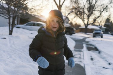 Child playing outside in winter snow during sunset clipart