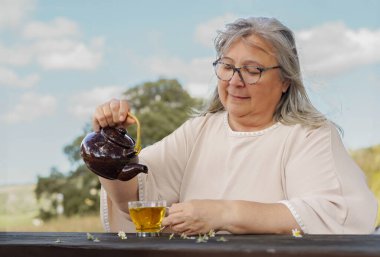 Bir fincan doğal papatya çayını çaydanlıkla dolduran kadın.