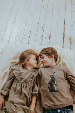 Bir erkek ve bir kız yatakta uzanıp birbirlerine bakıyorlar ve gülümsüyorlar.