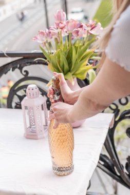 A girl opening a bottle of rose wine on a balcony in Budapest clipart