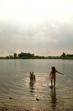Alman çoban köpeğiyle gölde koşan mutlu küçük kız.