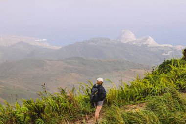 Sırt çantalı bir kadın yürüyüşçü tepede duruyor.