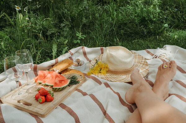 Female feet at a picnic with food  wine glasses  straw hat
