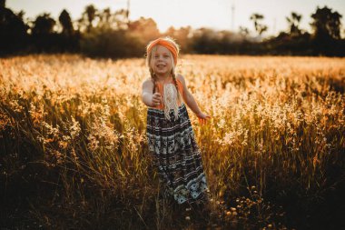 Turuncu elbiseli genç kız altın ışıkla tarlada duruyor.