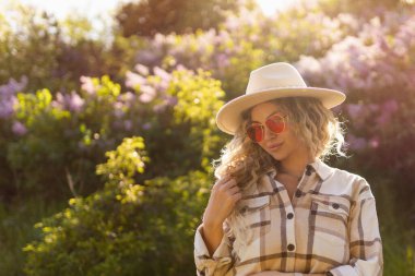 Seksi kıvırcık sarışın kameraya bakıyor, gözlüklü ve şapkalı.