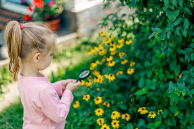 Bir çocuk büyüteç altında bir çiçeği inceler.