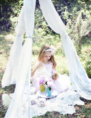 Bahçede dantel bir gölgelik altında kedi yavrusuyla oynayan bir kız..