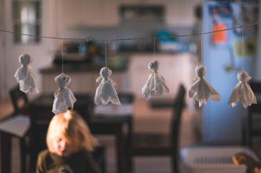 Small ghost decorations hanging on a string indoors with a child clipart