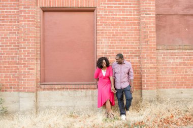 Kırmızı tuğladan duvara yaslanan çift gülüyor.