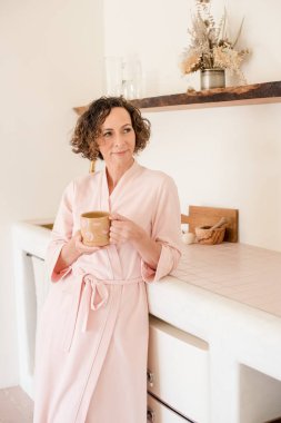 Pembe bornozlu, elinde bir fincan kahve tutan gülümseyen kadınlar.