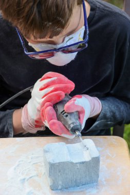 Gençlik koruyucu giysiler giyip taş bloğu elektrikli bir aletle oyuyor.