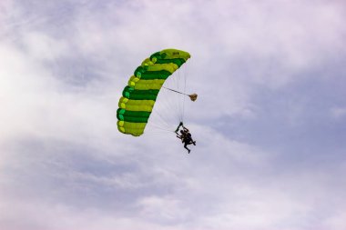 Skydivers gliding down with a green parachute in an overcast sky. clipart