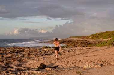 Hawaii 'de gün batımında kayalık bir sahilde yürüyen bir kadın..