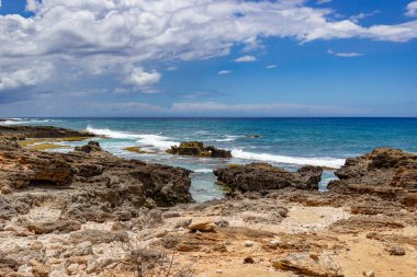Hawaii 'de açık mavi gökyüzü ile kayalık kıyılara vuran dalgalar.