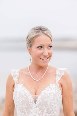 İnci kolyesi ve küpeleriyle dantelli gelinlik içinde gülümseyen gelin.