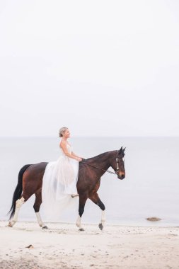 Dantel gelinlikli gelin kıyı şeridi boyunca ata biniyor.
