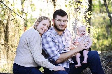 Ebeveynler bebekle birlikte güneşli bir ormanda oturur, bakıp gülümserler.