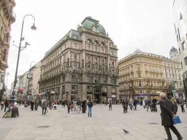 Tarihi binaları ve modern dükkanları olan kalabalık şehir meydanı.