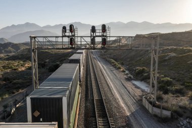 Stack train passing under signal bridge in landscape clipart