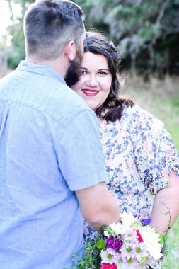 Elinde buket tutan, kameraya bakan hamile bir kadın.