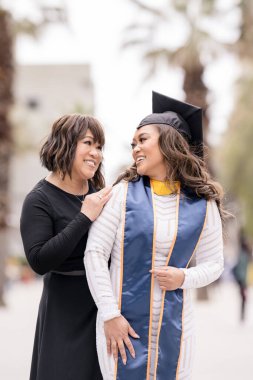 Mother of graduate looking into daughters eyes smiling clipart