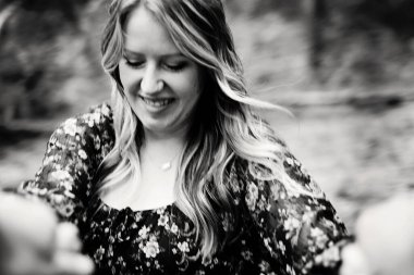 Dalgalı saçlı, çiçekli elbiseli, gülümseyen kadın.