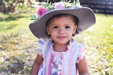 Toddler in a colorful dress and hat with flowers, smiling outdoo clipart