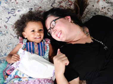 Woman and girl lying on patterned rug, smiling, holding wipes. clipart