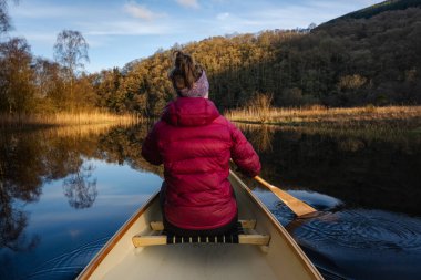 Woman paddling canoe on calm water clipart