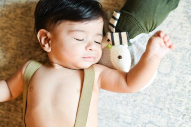 Baby sleeping on a soft surface with a stuffed toy beside them. clipart