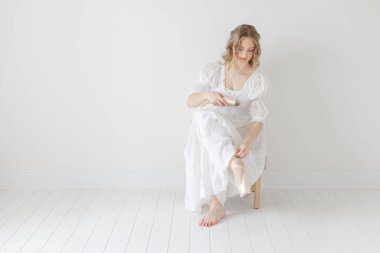 Balerin, beyaz stüdyoda sivri ayakkabılarını çıkarıyor.