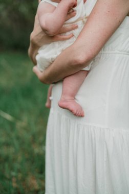 Anne beyaz elbiseli bebeği kucağında tutuyor..