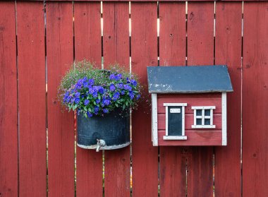 Kırmızı bir çitte, çiçekli ve posta kutulu bir yaz süslemesi.