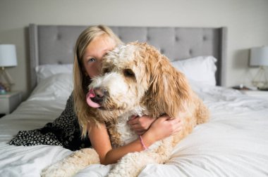 Pre-teen girl and fluffy dog lay on a bed clipart