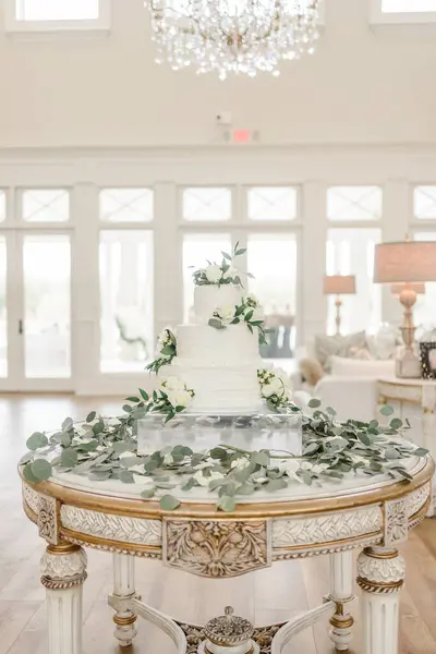 stock image White wedding cake with eucalyptus accents inside under chandelier