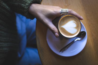 Kahve dükkanında elinde sütlü kahve tutan bir kadın.