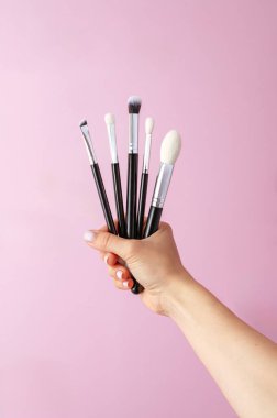 Bir kadının eli makyaj fırçalarını tutar.