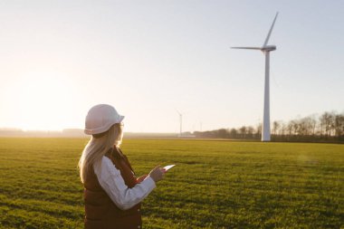 Kadın mühendis rüzgar türbini çiftliğinde çalışmak için tablet kullanıyor.