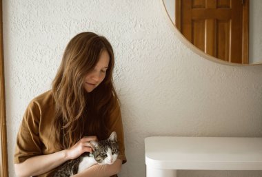 Oturan kadın kediyi kucağında tutuyor. İçi fotokopi alanıyla dolu.