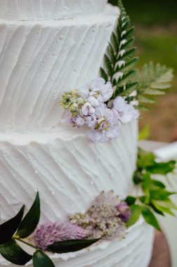 Üzerinde mor çiçekler ve yeşil yapraklar olan 4 katlı beyaz düğün pastası.