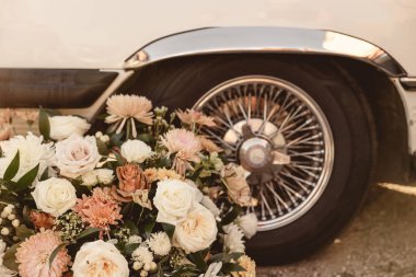 Sıcak pembe ve beyaz çiçek aranjmanı, klasik araba tekerleğinin yanında.