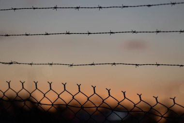 Günbatımı gökyüzüne karşı dikenli tel örgü örülmüş