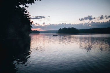 Alacakaranlıkta sakin bir göl, siluetli ağaçlar ve bir ada..