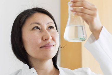 Asyalı kadın cam şişeyi kontrol ediyor.