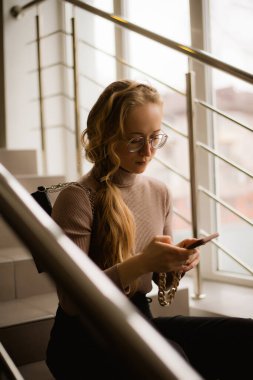 Gözlüklü genç bir kadın merdivenlerde oturuyor.