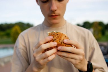 Açık havada sandviç yiyen bir gencin ellerine odaklan.