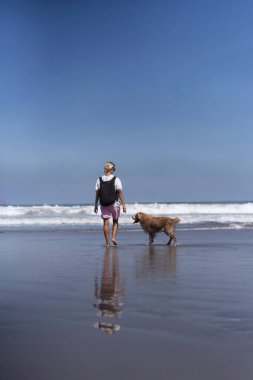 Golden retriever köpeğiyle sahilde yürüyen bir kadın..